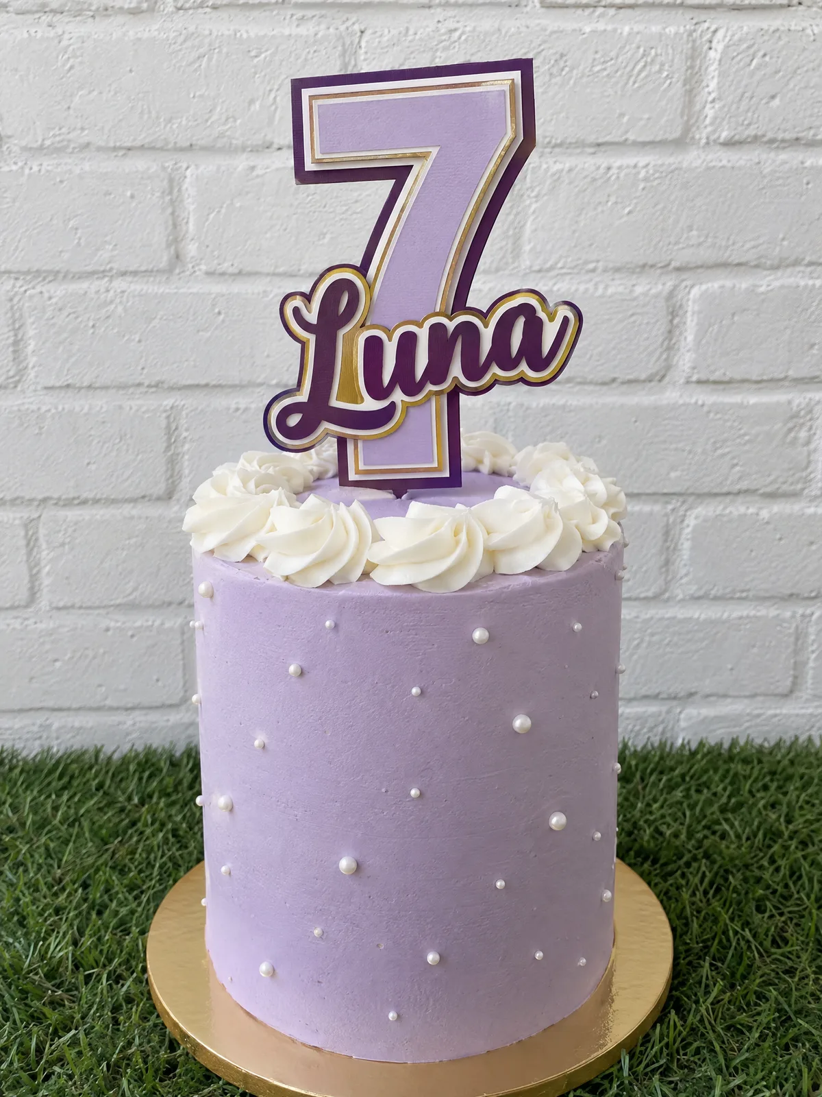 Torta lila con perlitas y un cake topper de cartulina en capas: un 7 grande con el nombre Luna en cursiva