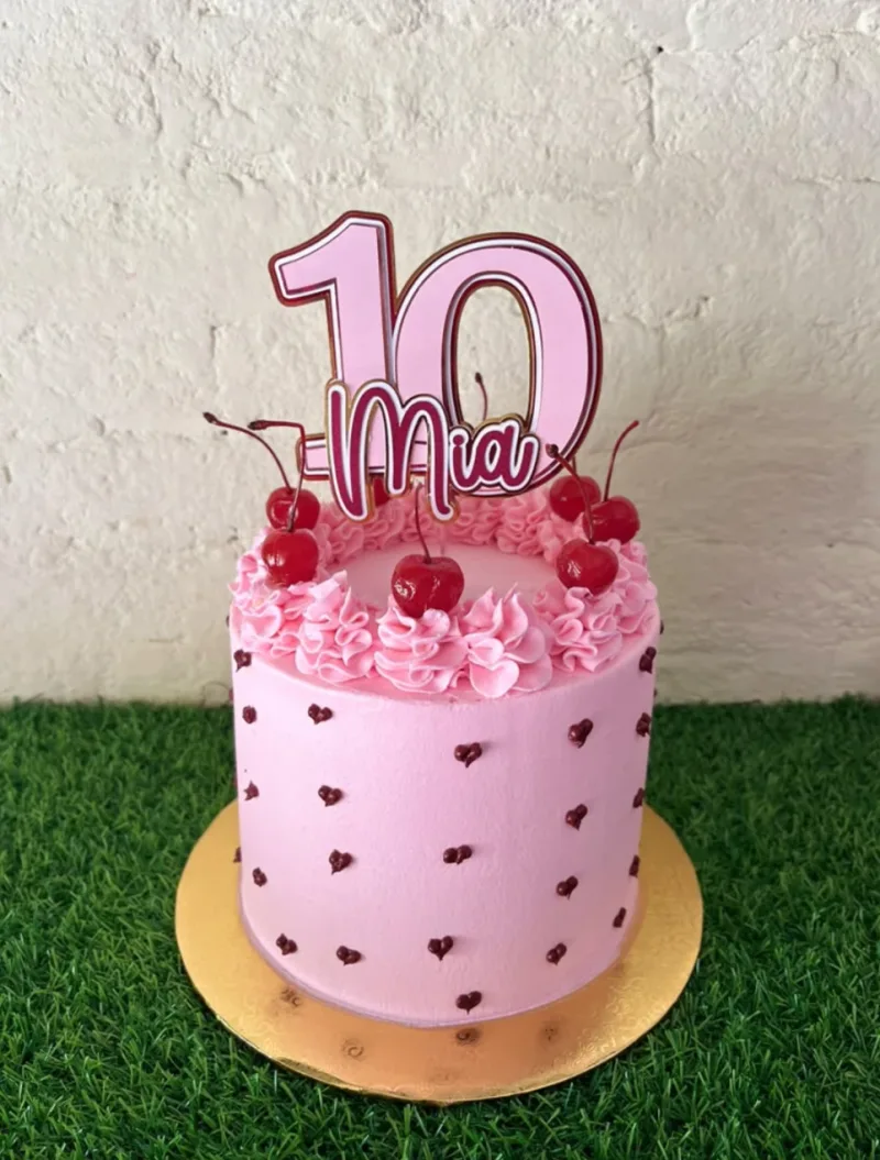 Pedido real: torta rosada con cerezas y un cake topper de cartulina en capas que dice Mia 10